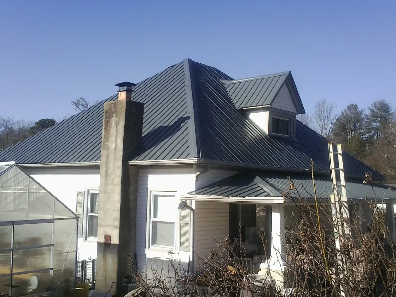 Dark blue standing seam metal roof on a white farmhouse with dormer — Slate & Tile Roof Repair by Roofing Brothers in Islandton