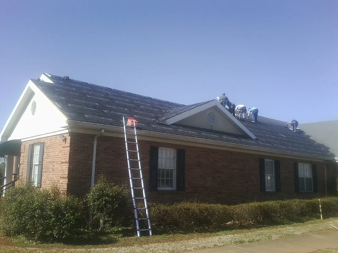 Crew tearing shingles off a brick ranch roof with a ladder set — Emergency Roof Repair work by our crew in Islandton
