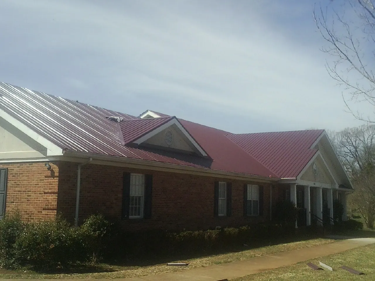 Red metal roof with gabled entries on a long brick building, from a Hail Damage Roof Repair job in Islandton