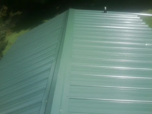 New green metal panels meeting at the ridge of a roof — Flat Roof Repair work by our crew in Islandton