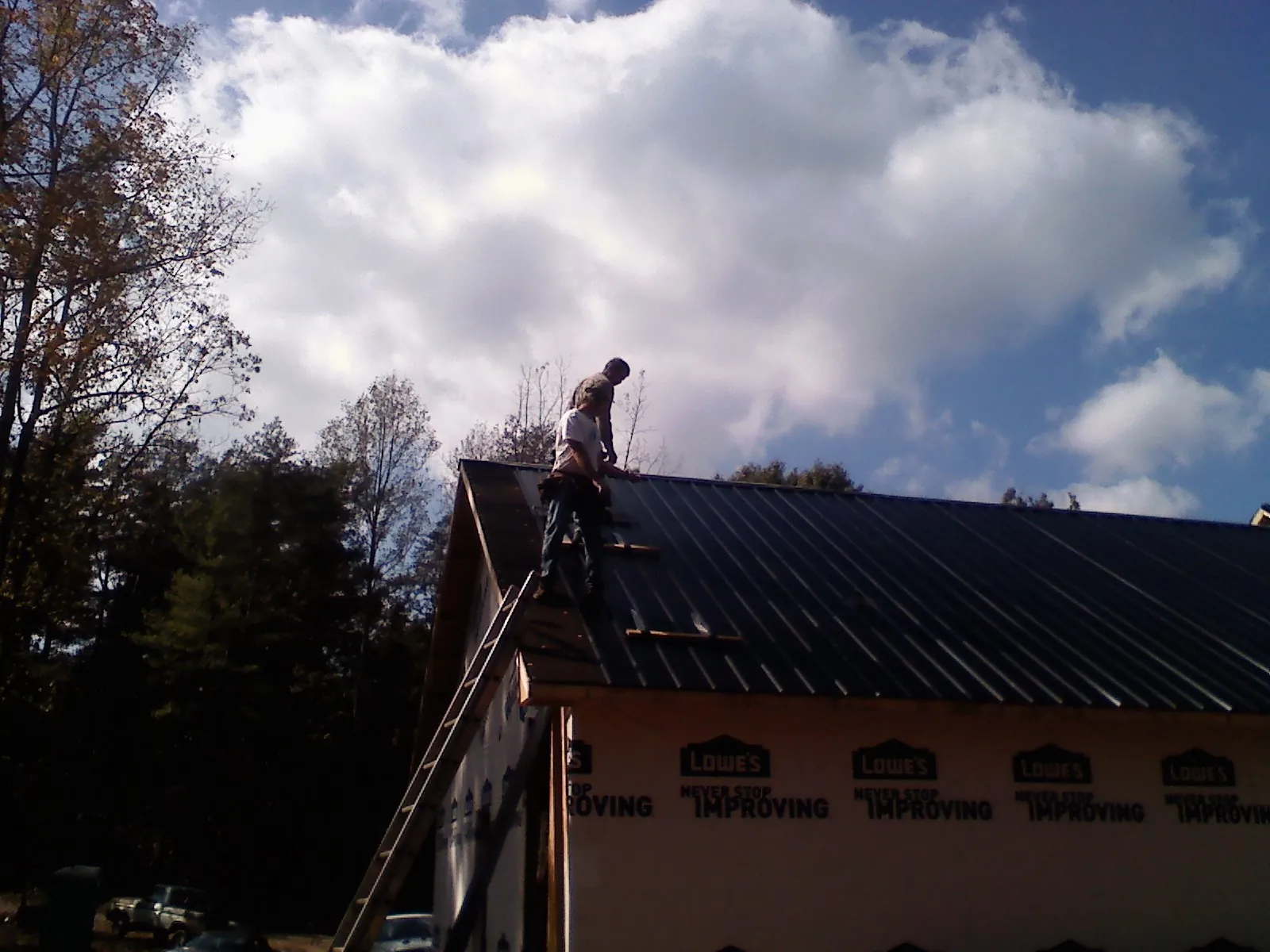 Roofer fastening dark metal panels high against a cloudy sky, from a Roof Inspection job in Islandton