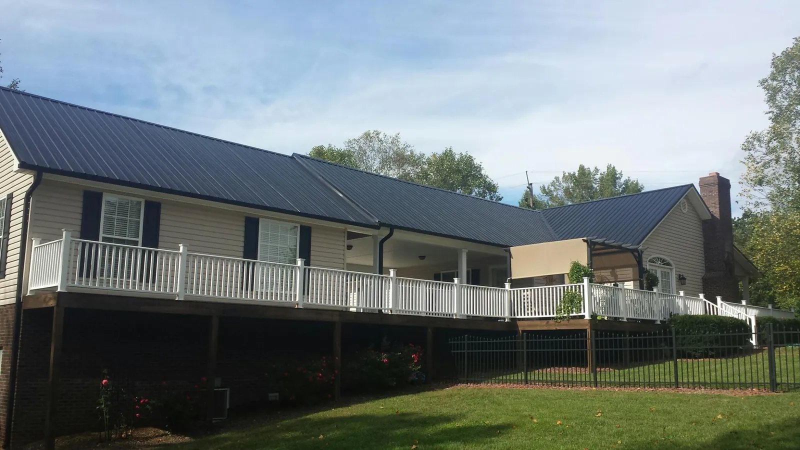 Black metal roof above a long white railed deck on a hillside home in Islandton