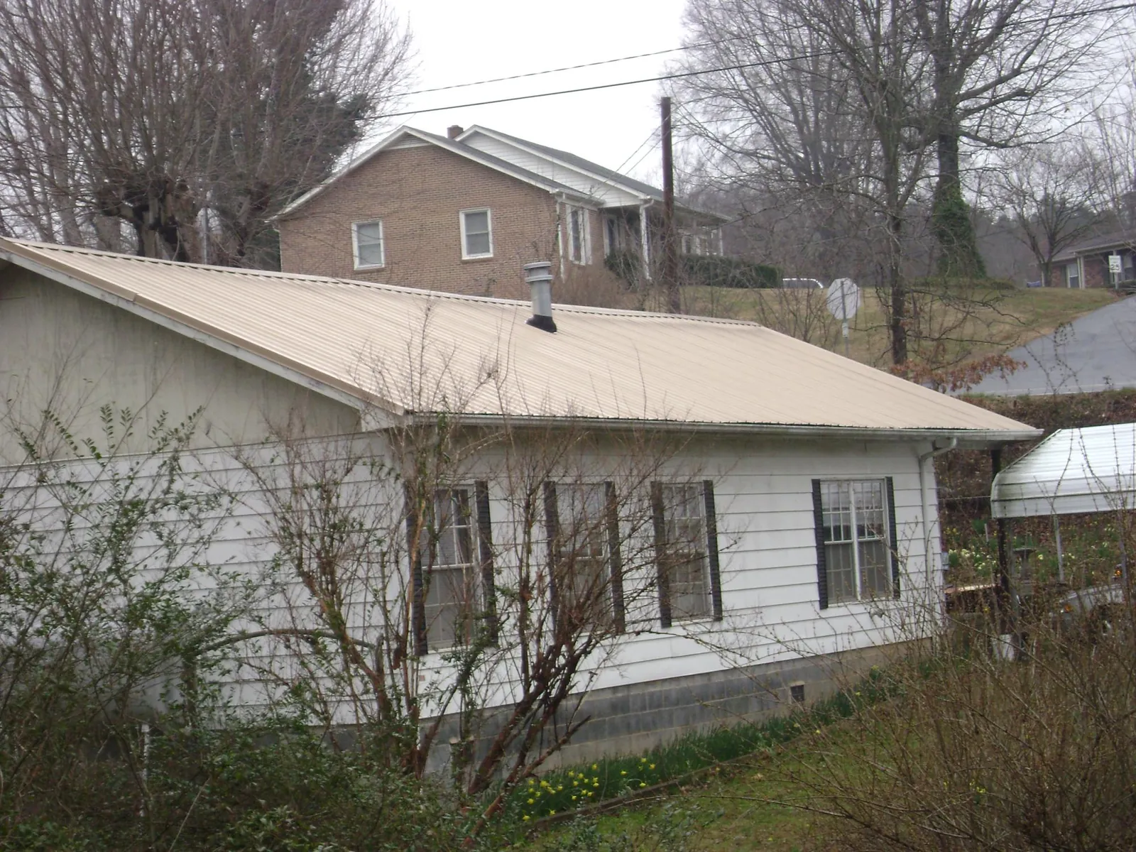 Tan metal roof on a white sided house set into a hillside — Commercial Roofing by Roofing Brothers in Islandton
